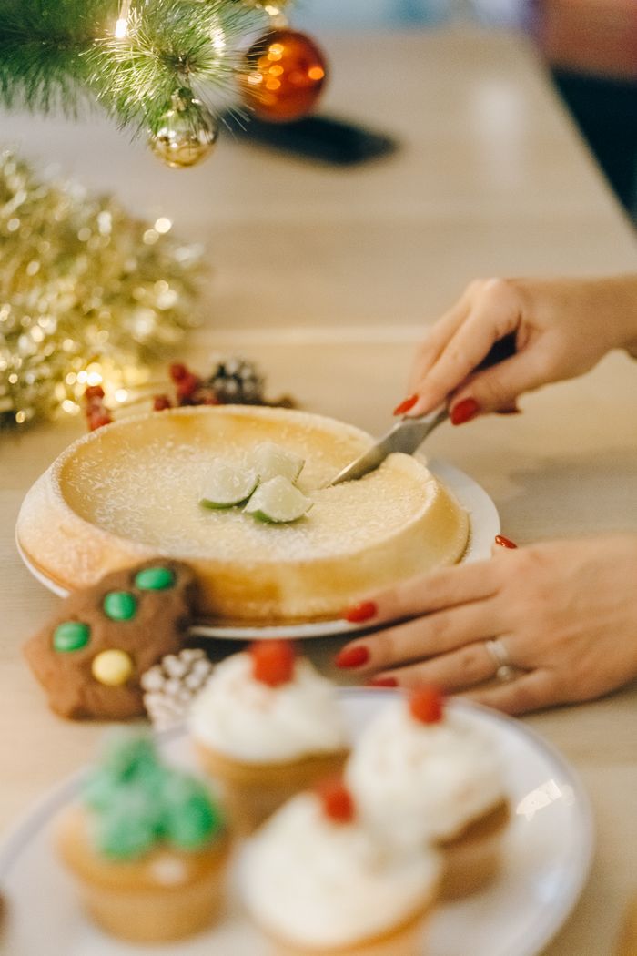 gallery-1 Close-up of a person slicing homemade cake with holiday decorations on a cozy table.