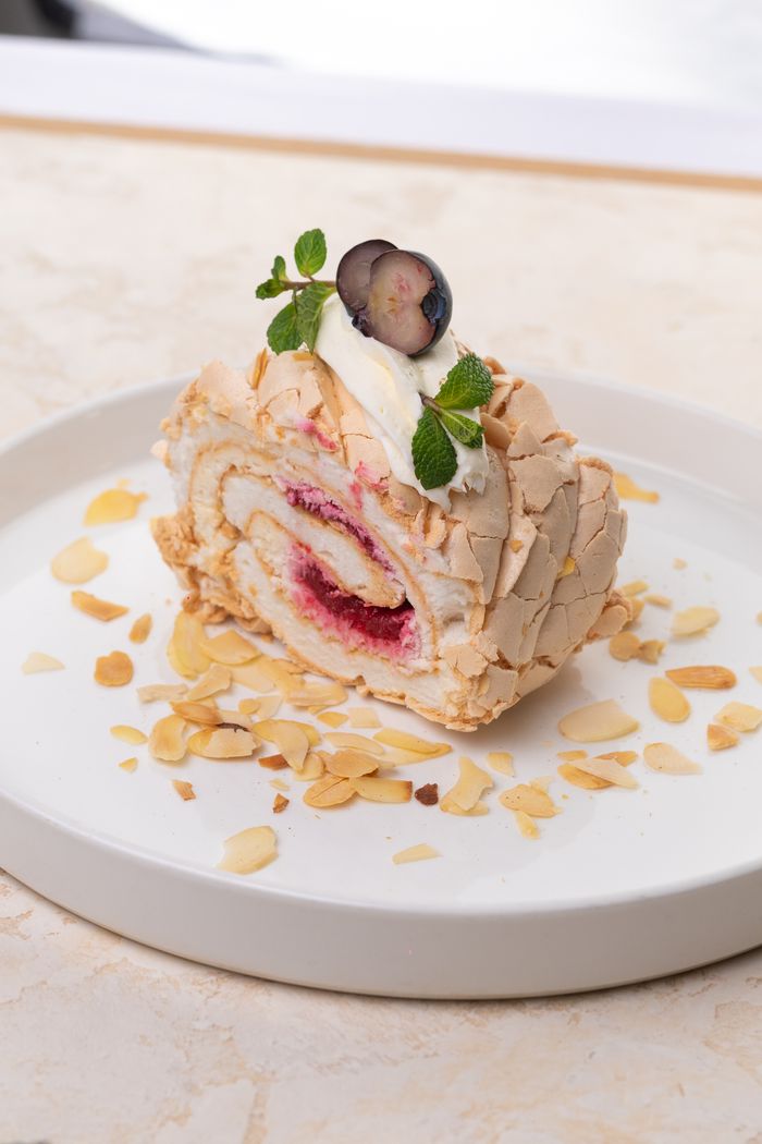 gallery-2 Mouth-watering meringue roulade topped with berries and cream, set on a white plate.