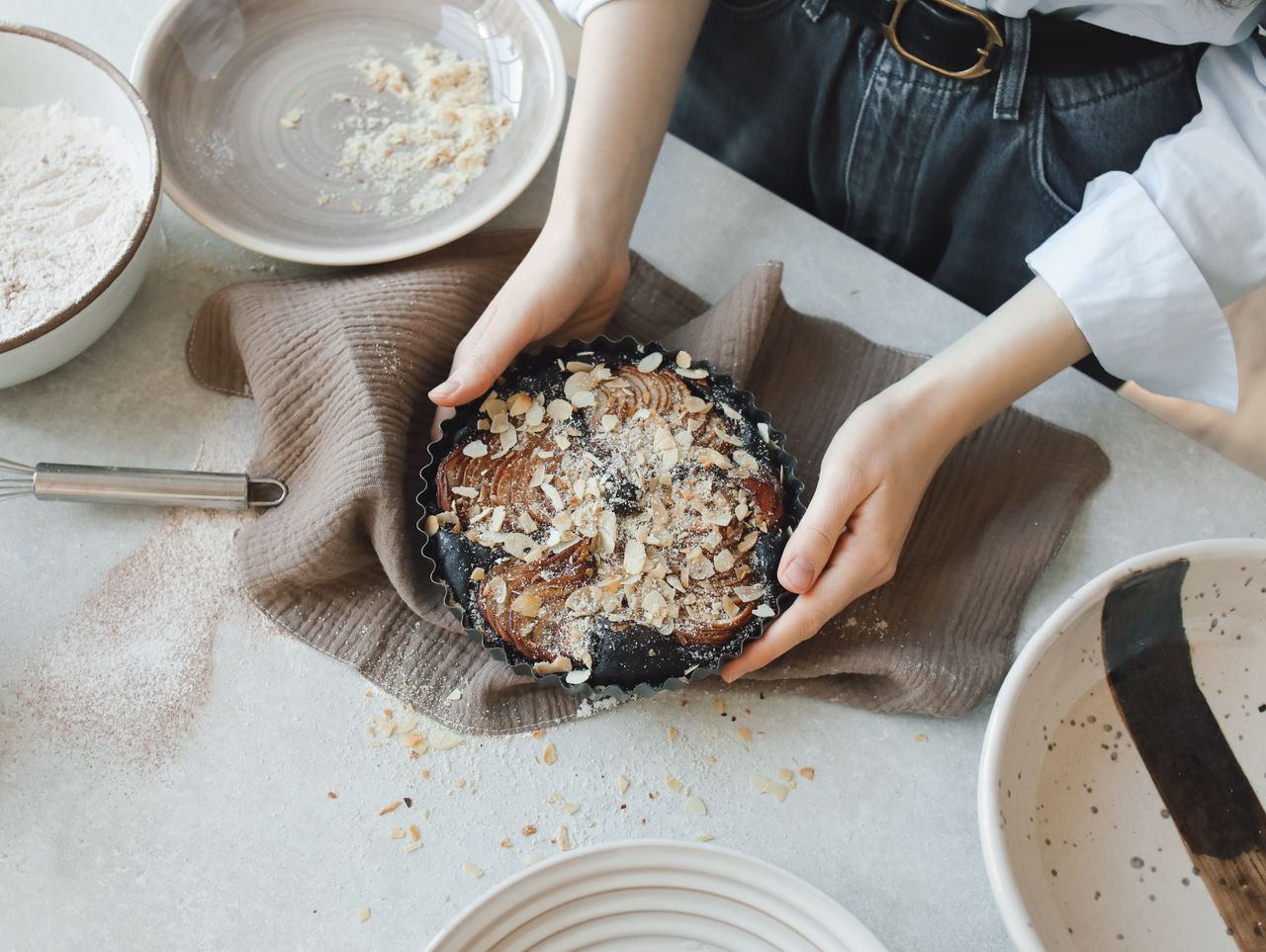 Top view of a woman holding a freshly baked almond cake in her kitchen.